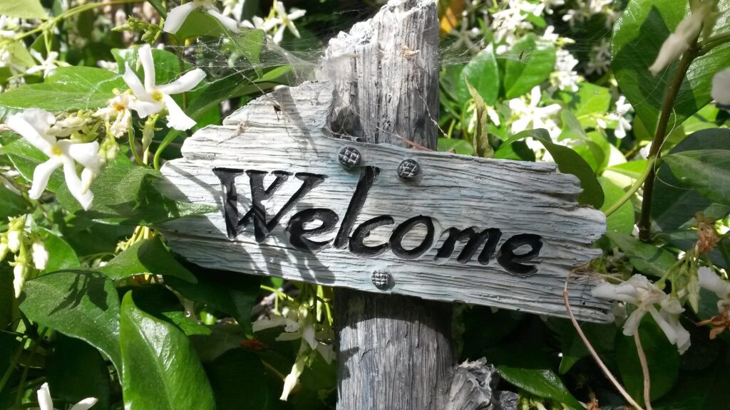 a garden sign inscribed with the words "welcome" among green leaves and white flowers