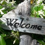 a garden sign inscribed with the words "welcome" among green leaves and white flowers